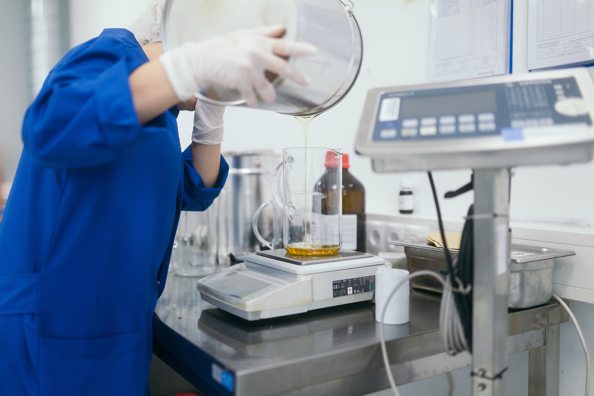 Foto aus dem Hanfama Labor: Öl wird von von Person mit blauem Kittel und weißen Handschuhen auf einer Waage abgefüllt